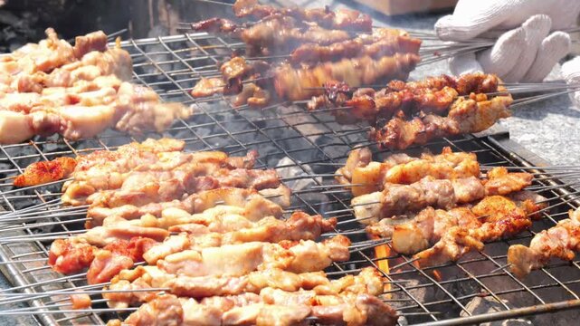 A wide shot of numerous meat skewers grilling on a large outdoor charcoal barbecue rack with a cook.