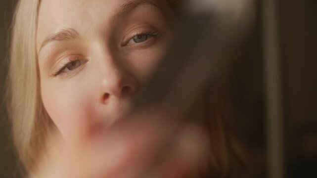 Close up shot of blonde gen Z Caucasian woman with gray eyes looking at crystal prism in morning sunlight indoors