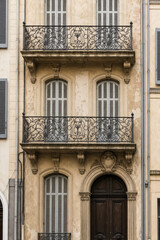 Obraz premium Close-up of a historic building facade with ornate wrought-iron balconies, arched entry, and sunlit beige stone, featuring symmetrical windows and classical architectural details.