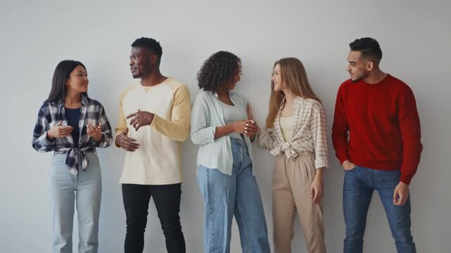 A group of five friends stands close together in a studio. They are engaged in a lively conversation and sharing smiles. This gathering showcases diversity in gender and ethnicity.