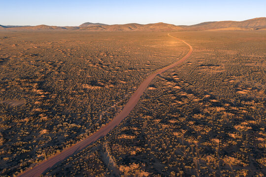 Aerial view of a winding dirt road stretching through the vast arid outback landscape with rolling hills during golden hour in Flinders Ranges, South Australia, Australia.