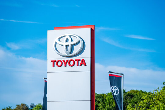 Toyota dealership sign with red logo and silver emblem, blue sky, dealer network analyses, EV transition reports, Japanese automaker, car sales, automotive industry, outdoor signage Eschborn, GERMANY