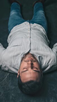 Man lying on floor with eyes closed in dark studio. Zoom in to close-up of face.