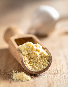 Dry garlic powder in wooden scoop, tasty spice for food, cooking and culinary concept, organic natural mood, blurred backdrop, minimal rustic styling. Close-up.