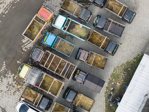 Aerial view of Animal Market Prambanan with small trucks parked on hexagonal pavement and beds filled with straw and hay in Kecamatan Prambanan, Jawa Tengah, Indonesia.