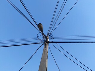 Fototapeta premium Tall utility pole with complex network of power lines against clear blue sky. Industrial infrastructure element creating strong geometric pattern and urban landscape feel.