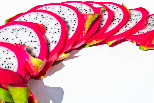 Top view of dragon fruit slices arranged in a long smooth curved line on a clean white background. 