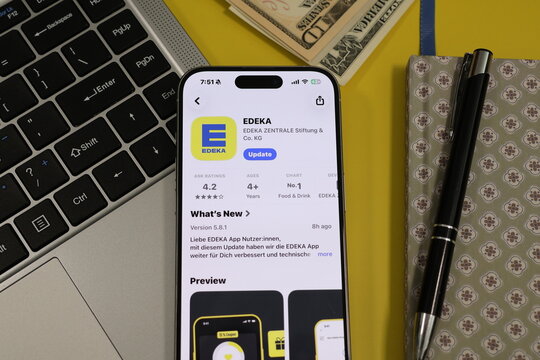 Kiel, Germany - 05-20-2026: Smartphone displaying the EDEKA grocery retail and supermarket app in the App Store in a workspace environment with laptop and notebook