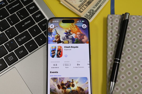 Kiel, Germany - 05-20-2026: Smartphone displaying the Clash Royale real-time strategy and multiplayer battle game app in the App Store in a workspace environment with laptop and notebook