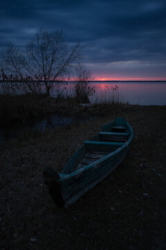 Sunset on the lake. Old rural wooden, fishing boat is moored on the shore of a lake.