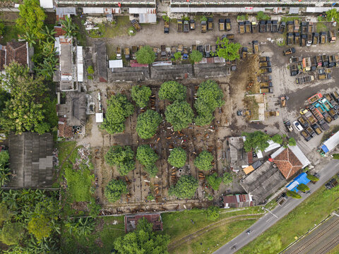 Aerial view of Animal Market Prambanan with trucks parked in rows, green trees, and traditional market structures in Kecamatan Prambanan, Jawa Tengah, Indonesia.