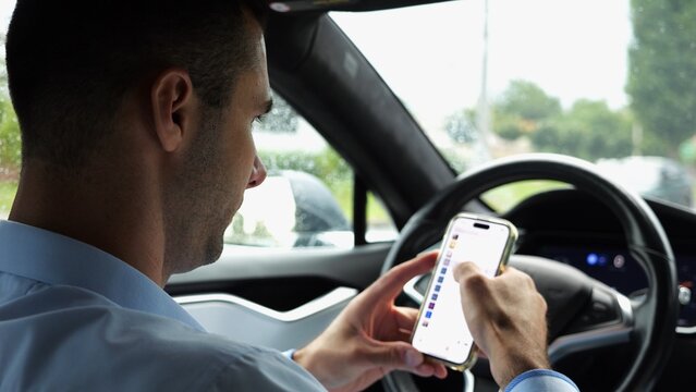 Male entrepreneur browsing modern smartphone while riding autonomous self driving electric car at city. Successful businessman using phone during riding on electrical auto with autopilot at rainy day