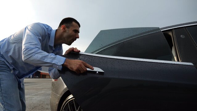 Successful smiling entrepreneur rejoices to purchase new electrical automobile at sunny rainy day. Happy young businessman in shirt enjoying modern electric auto. Concept of buy or rent car. Slow mo