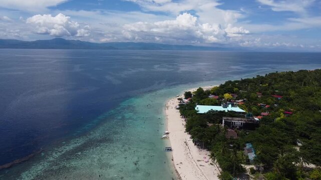 Drone aerial footage of White Beach in Moalboal, Cebu, Philippines featuring tropical coastline, ocean water, distant islands, jungle landscape and dramatic cloudy sky.