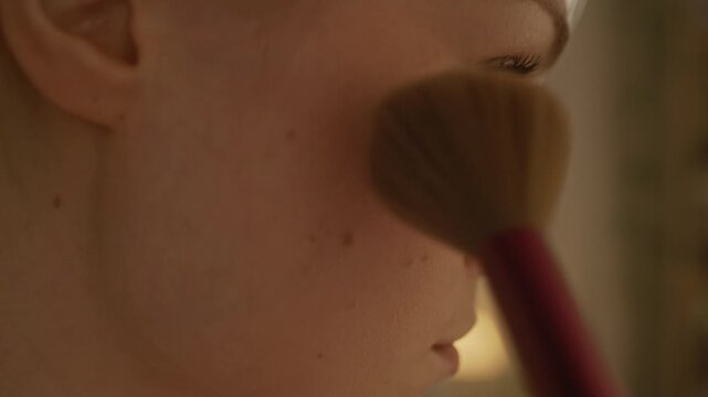 Close up side view of gen Z Caucasian girl using brush while applying blush on cheek during morning routine at home