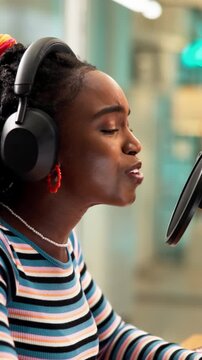 Woman, podcast and headphones in recording studio with microphone, pop culture news and discussion. Happy, black person and radio presenter talk with audio tech, live show or mainstream media update.