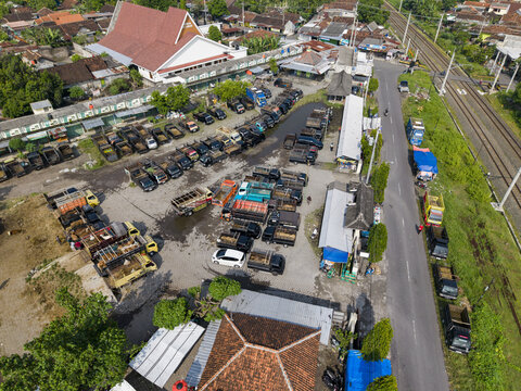 Aerial view of Animal Market Prambanan with trucks parked in the lot near a large white building and railway tracks in Kecamatan Prambanan, Jawa Tengah, Indonesia.