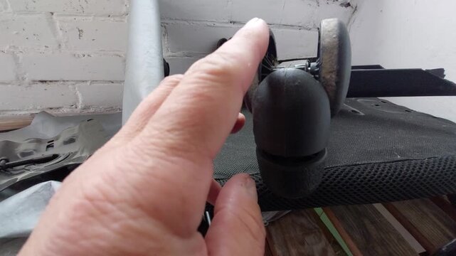 Hand inspecting and turning a dusty broken plastic caster wheel of an office chair close up
