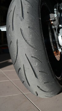 Closeup Motorcycle Rear Tire On Aluminium Swingarm And Chain, Parked In Gritty Garage, Mechanic Prepping Bike