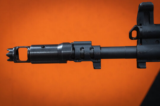 Detailed close-up of a tactical assault rifle barrel featuring a modern muzzle brake compensator, flash hider device, gas block, and front sight post