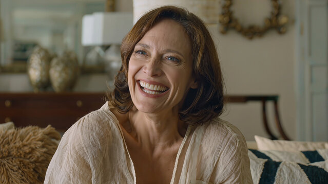 Portrait of cheerful mature woman laughing genuinely while relaxing on sofa at home