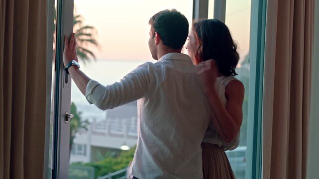 Sightseeing, couple and bonding in hotel, window and embrace with partner on honeymoon and vacation. Motel, view and happy people with hug on anniversary, support or connection on holiday with spouse