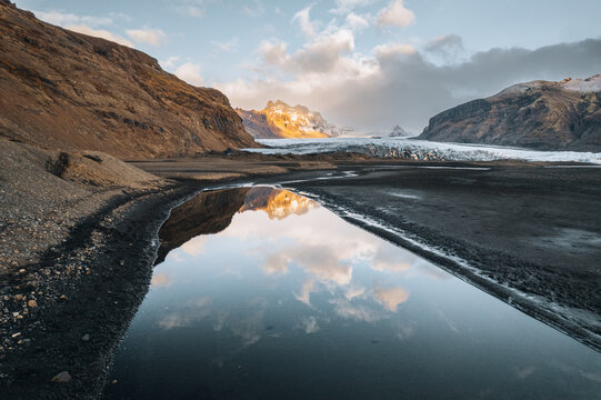 Aerial view of the Skaftafell glacier tongue and rugged mountains reflected in a calm pool of water during golden hour Skaftafell, Sveitarfelagid Hornaf, Iceland.