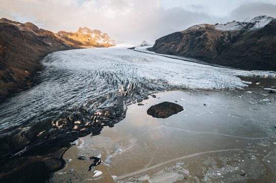 Aerial view of the Skaftafell glacier with its cracked ice surface and rugged mountain peaks under soft sunset light, Skaftafell, Sveitarfelagid Hornafjordur, Iceland.