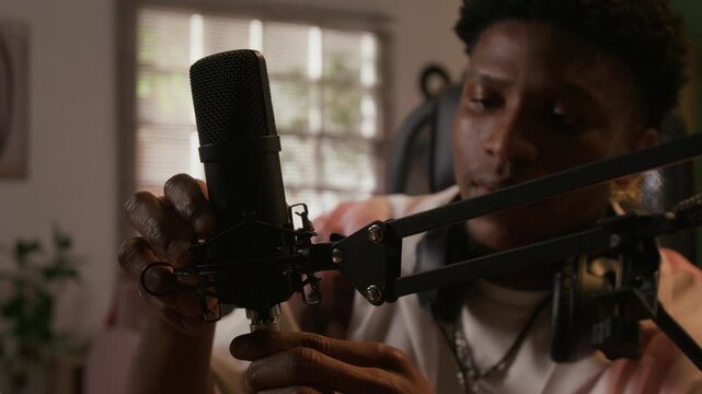 Close up shot of young adult Black male audio engineer plugging cable into microphone preparing equipment for music recording session in home studio