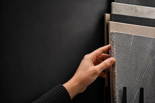 Hand selecting textured stone and tile samples on dark background for interior design material choice