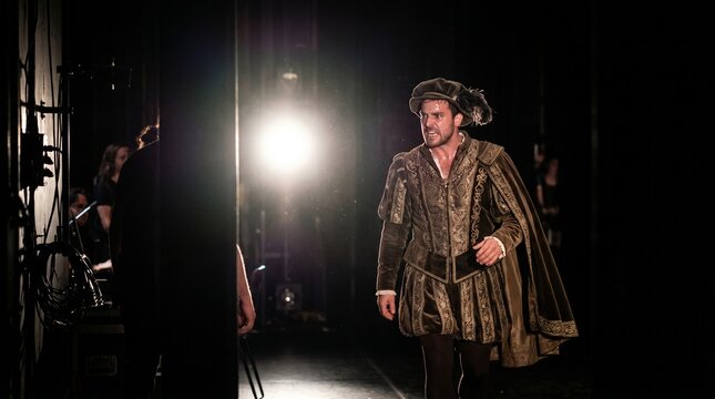 Actor performing on stage, wearing an elaborate historical costume and feathered hat, showing intense emotion. Theatrical performance and historical drama.