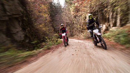 Fototapeta premium Motocross riders off-roading through autumn forest road