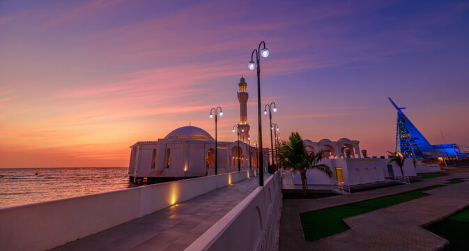 Al Rahmah (Floating) Mosque of Saudi Arabia, poised over the Red Sea at Jeddah city Corniche, glowing at sunset with vivid sky hues and mirror-like water reflections showcasing coastal serenity