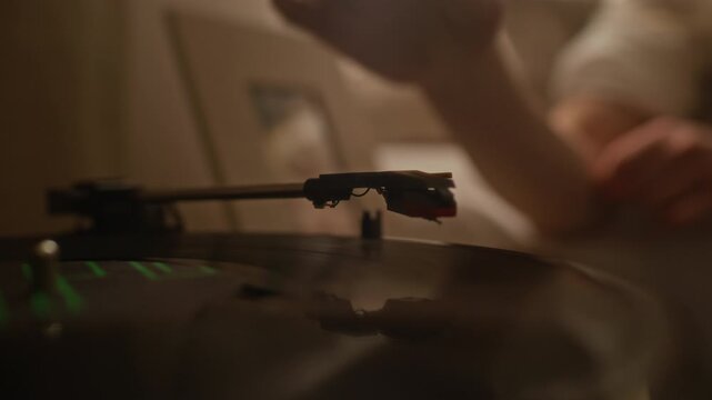Close up shot of hand of unrecognizable woman lowering needle onto spinning vinyl record on turntable while relaxing with music in bed during slow morning