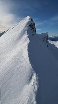 Aerial view of the sharp snow-covered ridge of Aiguille Croche mountain peak under a clear blue sky in the French Alps Les Contamines-Montjoie, Auvergne-Rhone-Alpes, France.
