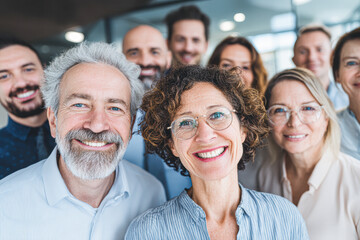 Fototapeta premium A group of smiling adults poses closely together, conveying happiness, teamwork, and a positive atmosphere in a modern indoor setting.