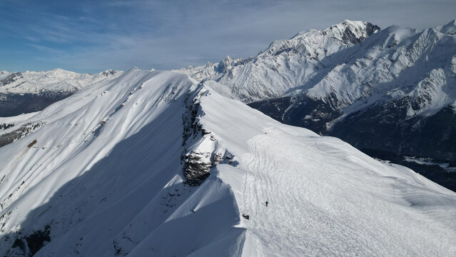 Aerial view of Aiguille Croche mountain ridge covered in snow with skiers on the slopes and the Mont Blanc massif in Les Contamines-Montjoie, Auvergne-Rhone-Alpes, France.