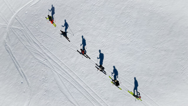 Aerial view of a group of skiers ascending a snowy slope near Pointe Percee with long shadows and tracks on the white snow Le Reposoir, Auvergne-Rhone-Alpes, France.