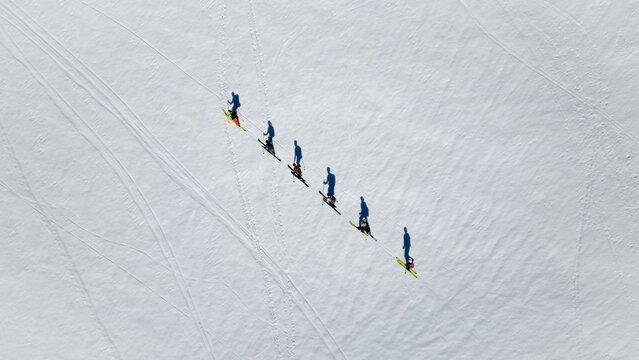 Aerial view of a group of skiers trekking in a line across a pristine snow-covered mountain slope with long shadows Le Reposoir, Auvergne-Rhone-Alpes, France.