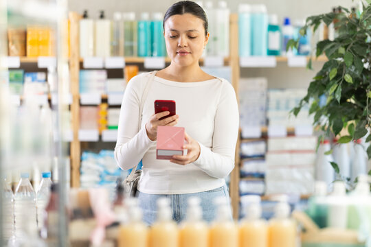 Calm and focused young Asian woman using smartphone to scan barcode on medicine box at pharmacy, checking authenticity and composition of prescribed product