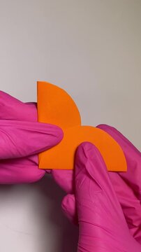 Vertical video of hands folding two small orange paper circles in half and layering them together. Simple paper craft process for handmade decorations, children's activities, and creative DIY projects