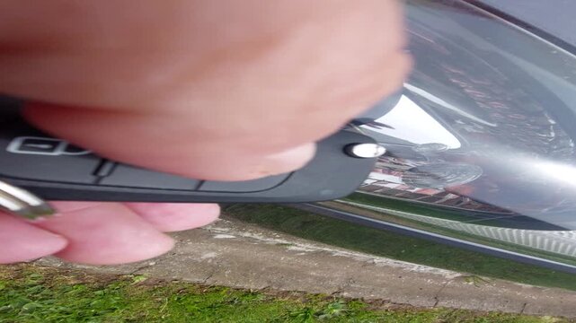 Hand pressing a remote key fob button to unlock a car with flashing indicator light vertical video