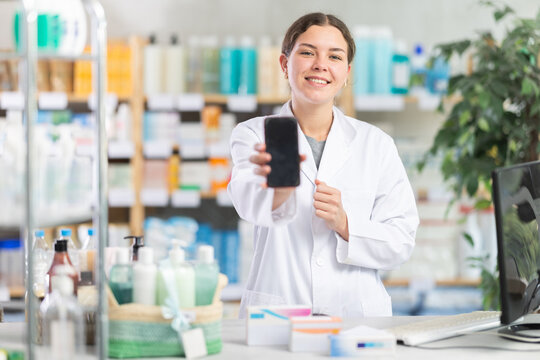 Woman pharmacist holds a mobile phone in her hands and offers to use an online application for ordering and paying in a pharmacy