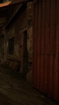 A view of an old building with a red door in a narrow street. The area is dimly lit and shows signs of wear. Some empty frames are seen on the ground near the door.