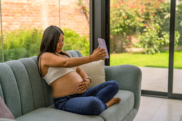 Obraz premium Pregnant woman taking selfie video calling in living room
