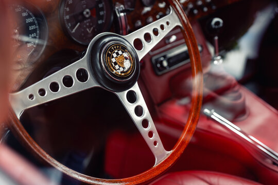 Leipzig, Germany - 9 May, 2026. Closeup view Jaguar E-Type steering wheel wooden rim chrome detail red leather interior vintage sportscar cockpit. Classic automotive design British engineering luxury