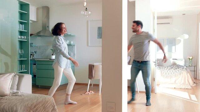 Playful, dancing and couple with laughing in home, weekend bonding and connection for relationship. Holding hands, funny partner and happy people with fun in apartment, support and moving to music