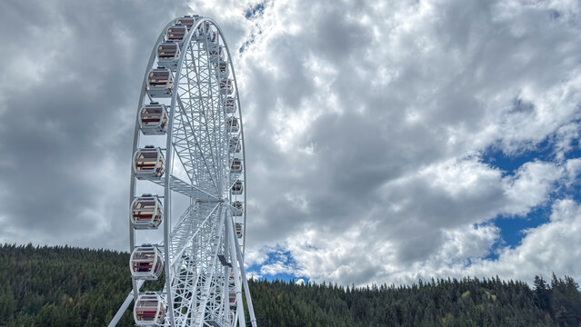 Giant Ferris wheel against a dramatic cloudy sky and forested mountain backdrop
