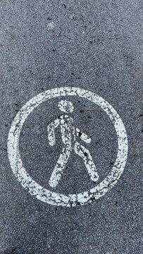 White pedestrian crossing symbol painted on asphalt pavement surface