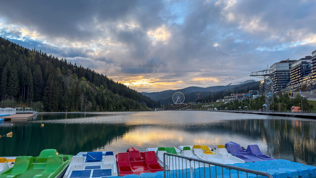 Scenic mountain lake with colorful paddle boats and modern resort buildings at sunset